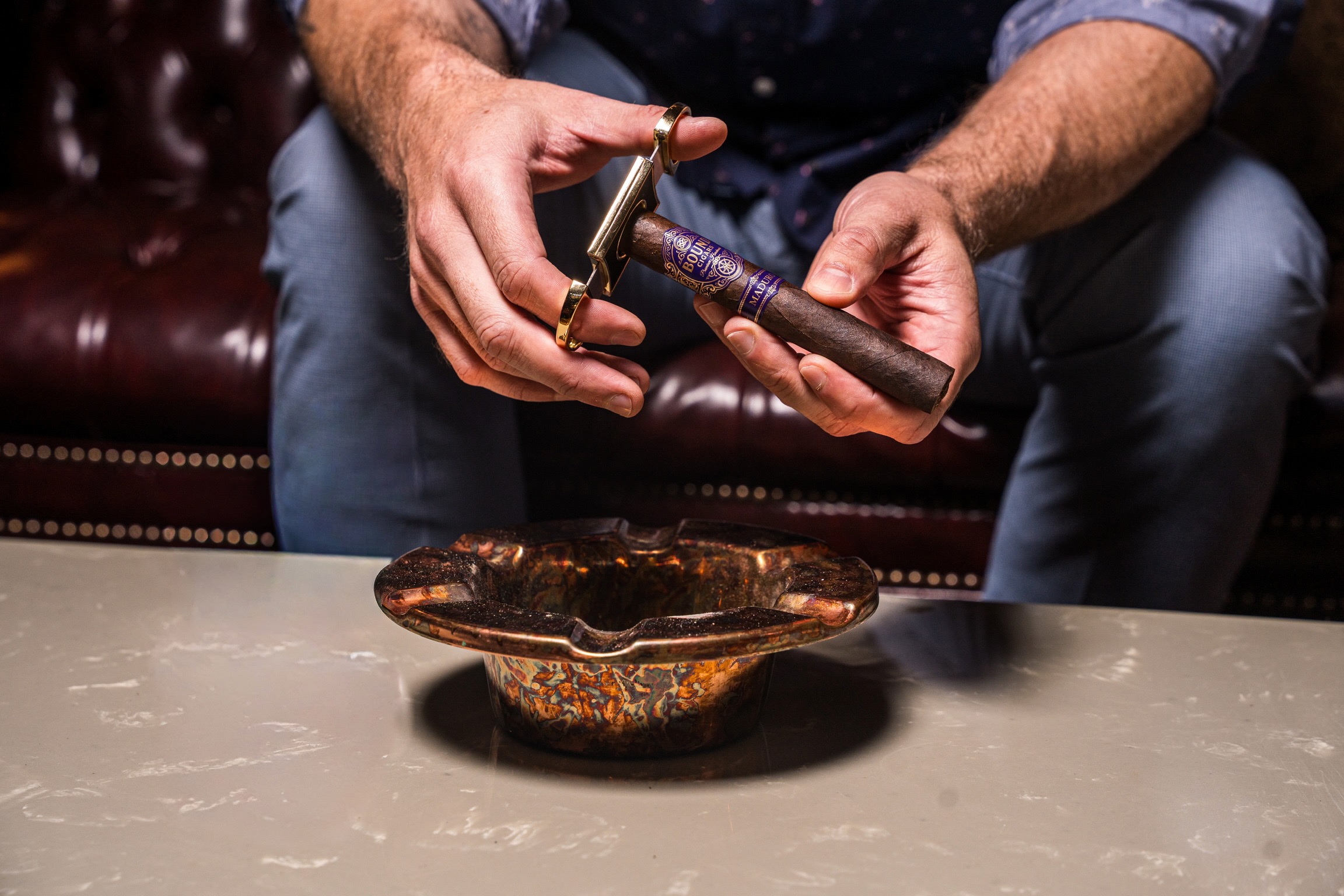 Hands using a cutter on a Bound cigar over an ashtray