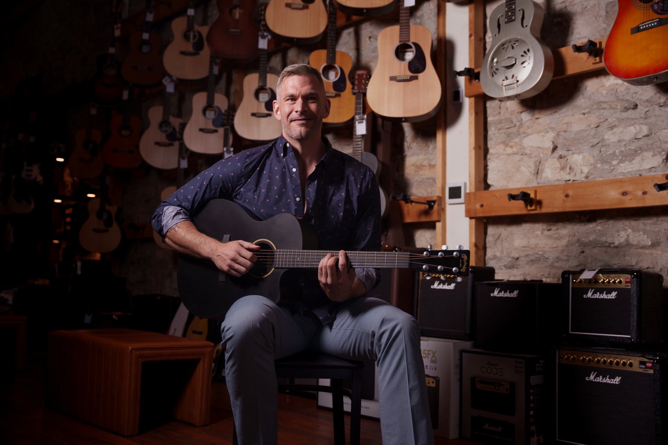 Drew Fowler playing guitar in front of a wall of guitars