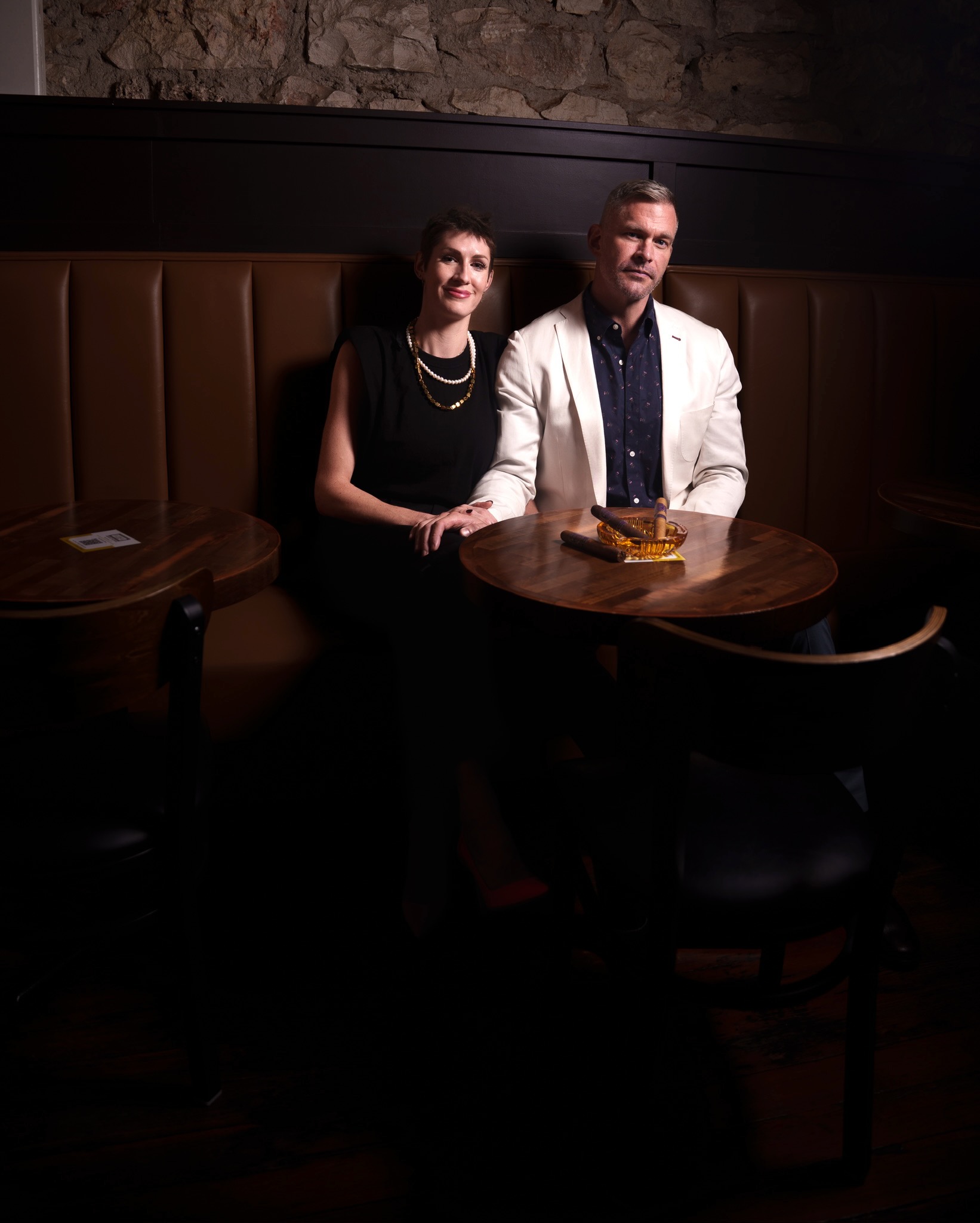 Kelly and Drew in a booth with cigars on the table