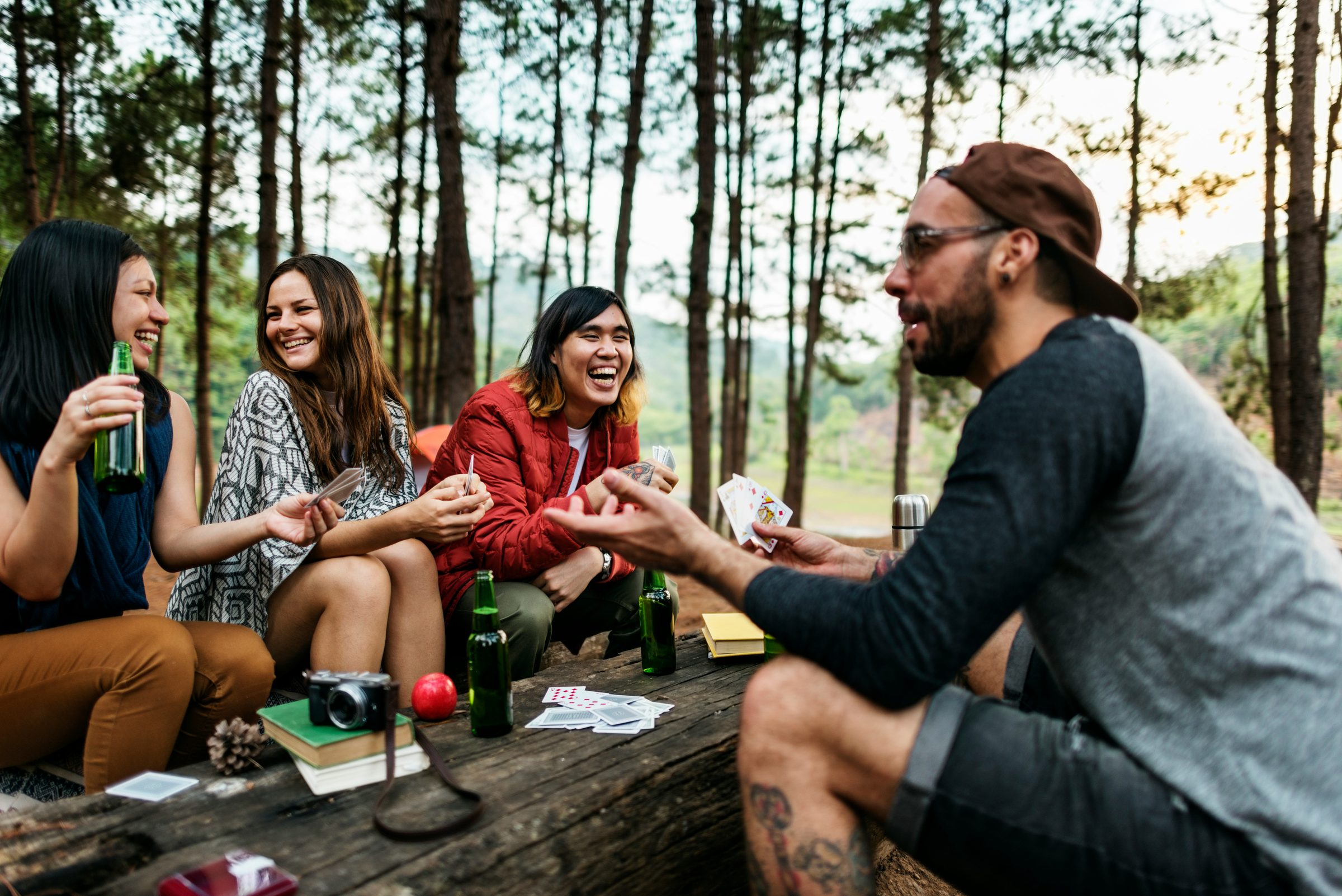 Friends playing cards around a picnic table among pines