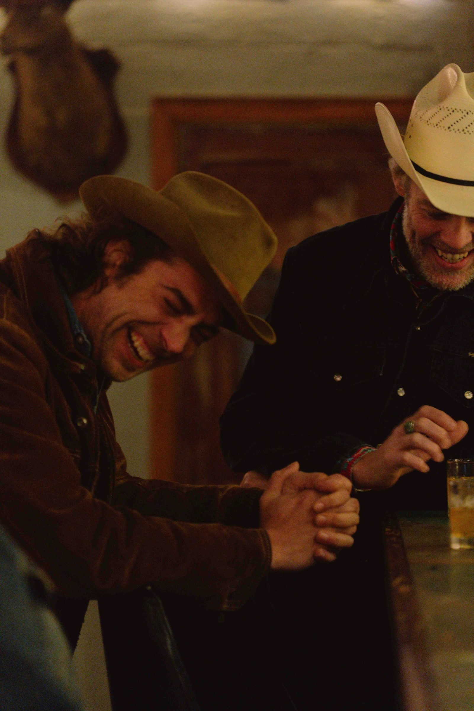 Two men laughing together in warm low light