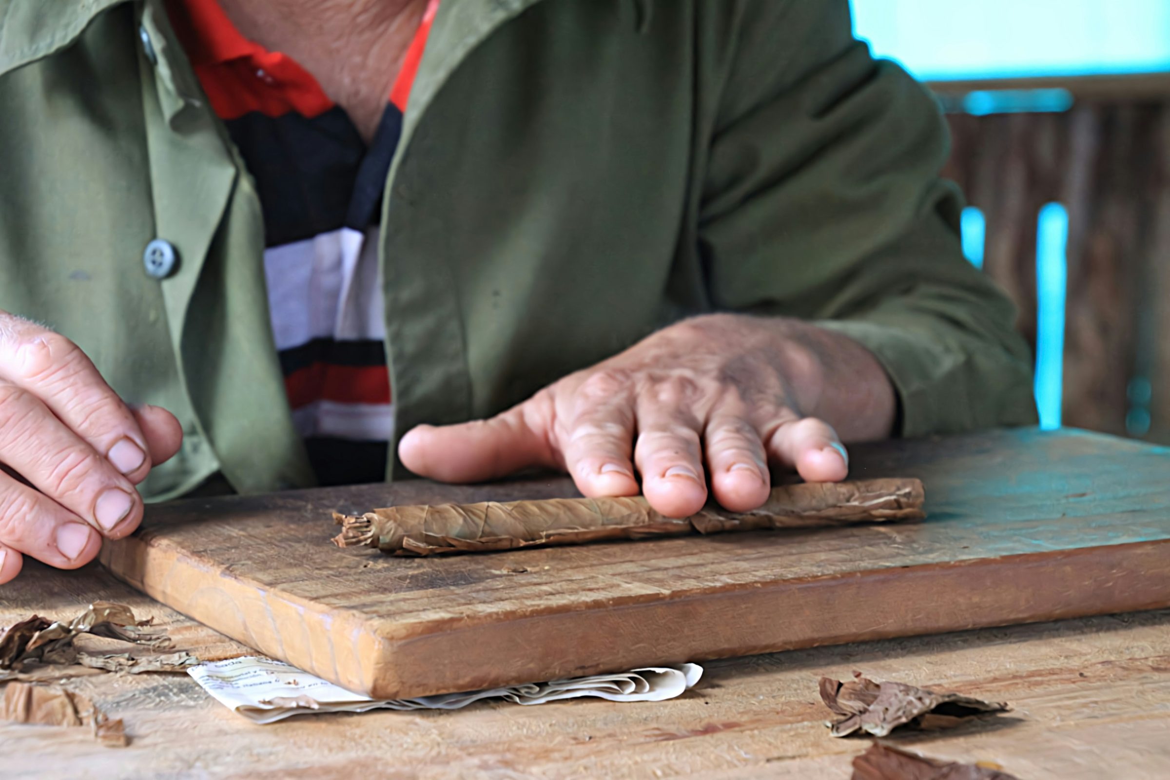 A torcedor rolling a cigar by hand on a wooden board