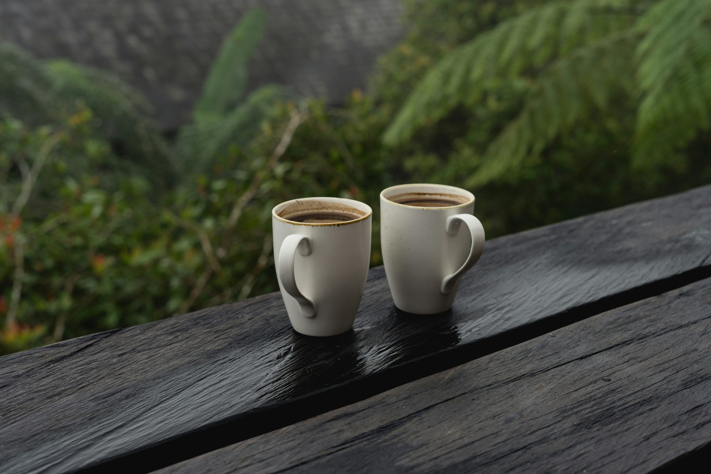 Two cups of coffee side by side on a weathered rail