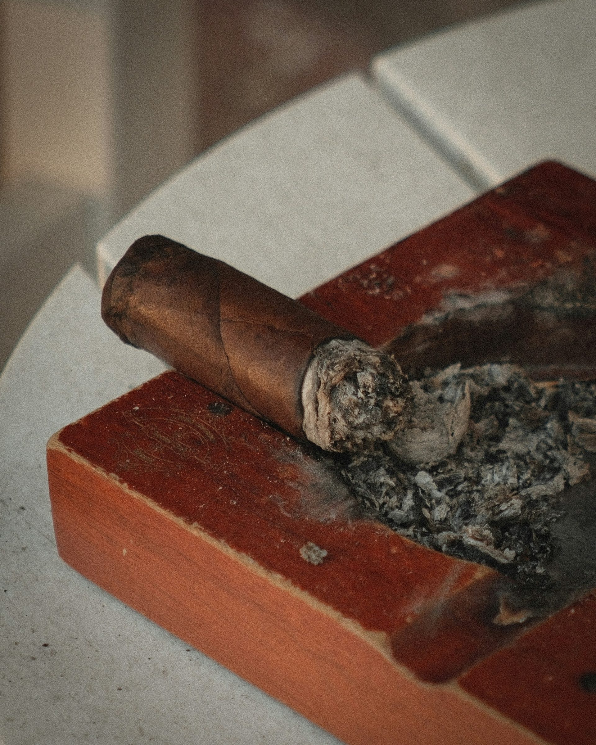 A lit cigar resting in a wooden ashtray with a long white ash
